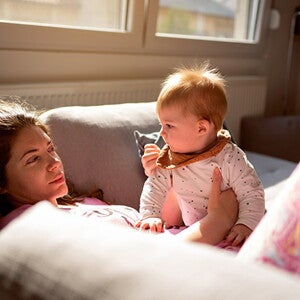 Moms lies on sofa, holding baby and looking dazed