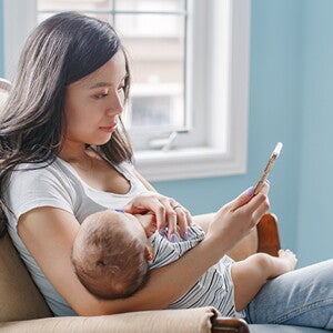 Mom sitting with baby in her arms looks at phone